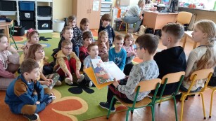 czwórka uczniów czyta książkę młodszym kolegom