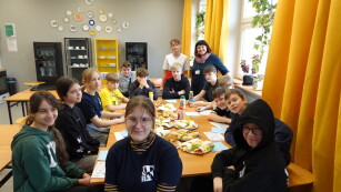 grupa uczniów siedząca wokół stołu zastawionego kolorowymi potrawami
