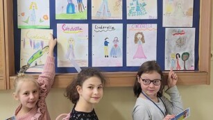 dziewczęta pokazują swoje prace w gablocie szkolnej na korytarzu