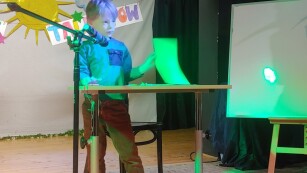 chłopiec stojący przy stoliku trzyma kartkę i nożyczki